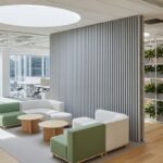 Bright open-plan office with Slatstone Lunarian grey stone wall panels, acoustic felt backing, natural wood floor, and modern lounge seating under daylight.
